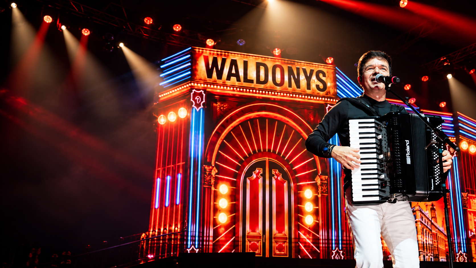 Waldonys tocando acordeão em um grande palco iluminado.